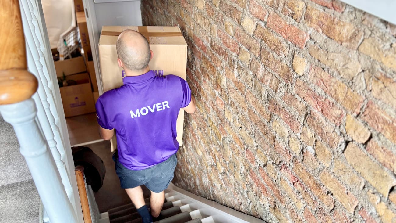 Professional mover carrying a packed box downstairs in a London property
